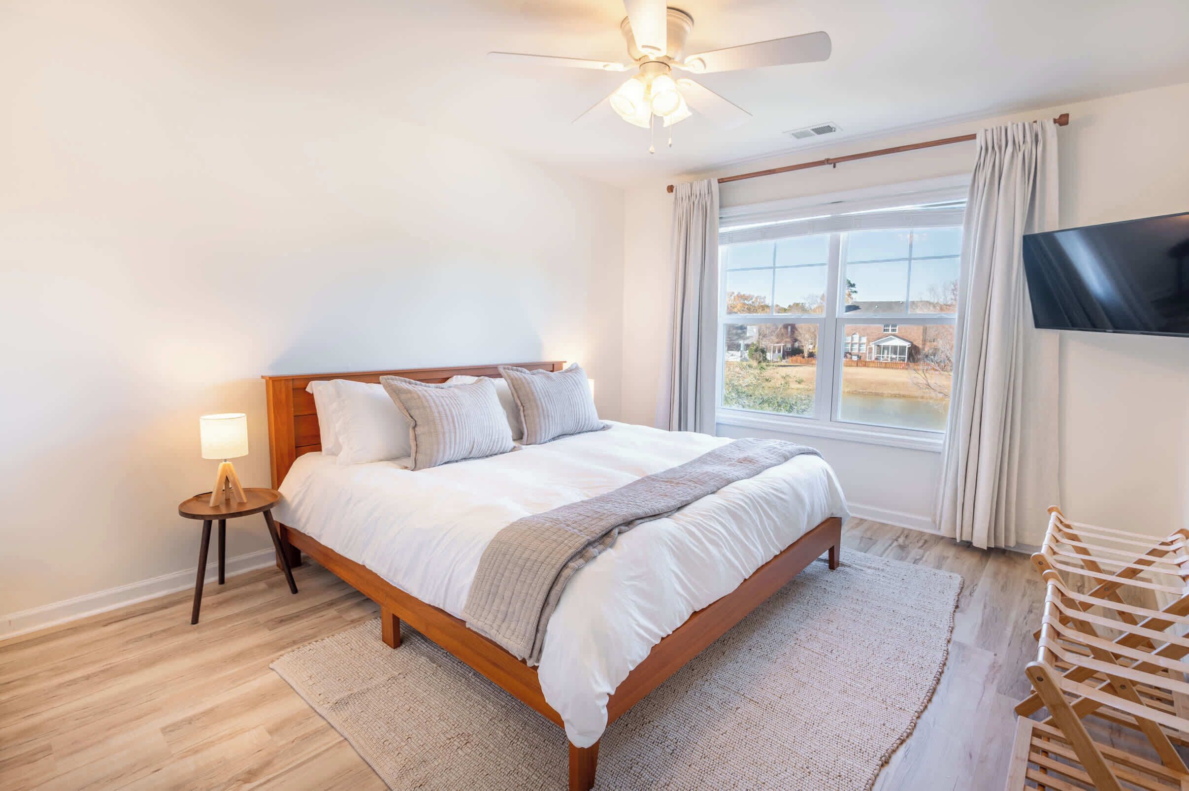 A bedroom with a bed, a ceiling fan, a TV, and a window with curtains.