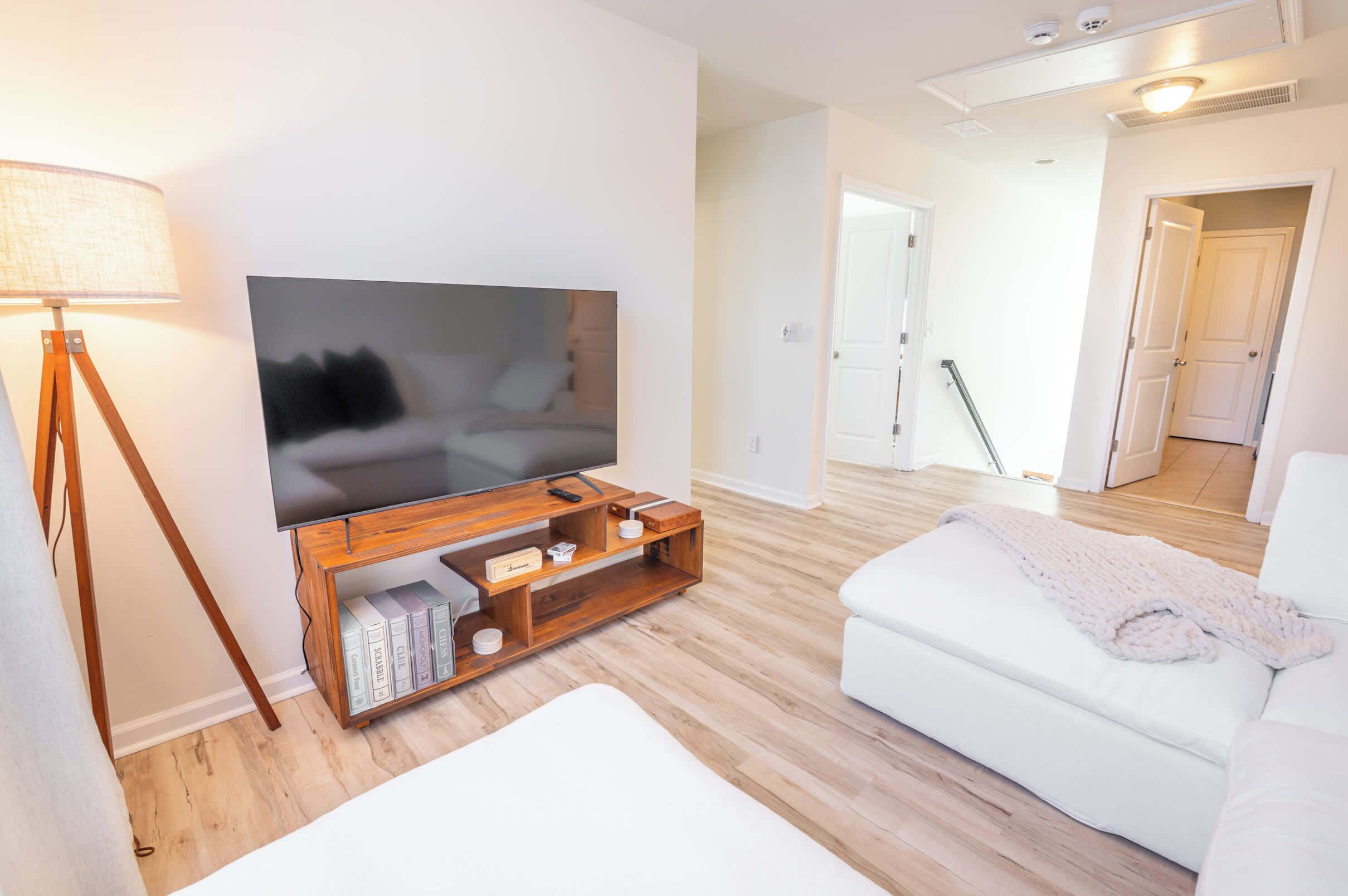 A modern living room with a flat-screen TV on a wooden stand, a white sofa, and a floor lamp.