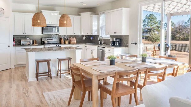 Una cucina moderna con mobili bianchi, un'isola centrale con sgabelli e luci a sospensione.