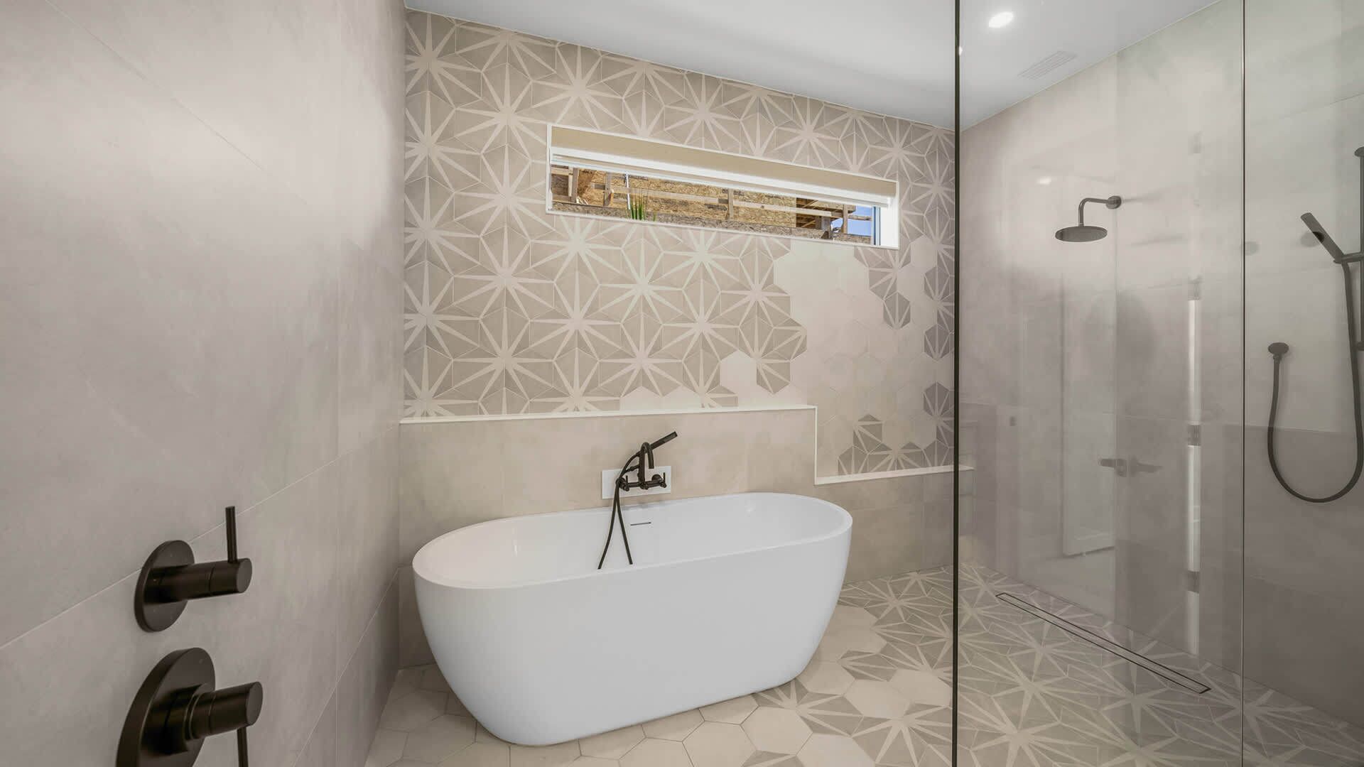 Un baño moderno con una bañera independiente, una ducha con cerramiento de vidrio y paredes con patrón geométrico.