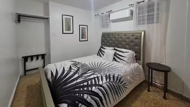 A bedroom with a bed, a bedside table, an air conditioning unit, and a door. - Unit 2@Casa Catalina-City, Culture, & Coastline (San Juan)