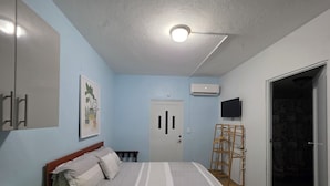 Un dormitorio con cama, armario, un cuadro, equipo de aire acondicionado y televisor.