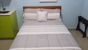 Una cama con un cubrecolcha a rayas, un cabecero de madera e ilustración de una planta colgada en la pared.