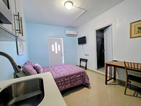 Ein Schlafzimmer mit Bett, Schreibtisch, Stuhl, Waschbecken und Fernseher.