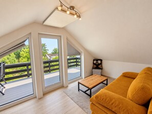 A room with a sloped ceiling, large windows, a wooden table, a sofa, and a ceiling light fixture.