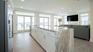 Una cocina moderna con armarios blancos, una isla de mármol y un amplio ventanal con vistas a un balcón.