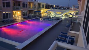 Un área de piscina con sillones de descanso y sombrillas, rodeada de edificios con balcones.
