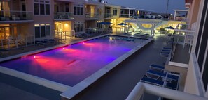 A pool area with lounge chairs and umbrellas, surrounded by buildings with balconies. - Top Floor Luxury 3BR Beach Condo with Bay Views (Dewey Beach)