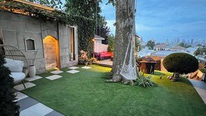 Dachterrasse mit Kunstgrasanlage, einer Hängematte, einem Baum und Blick auf die Stadtlandschaft.