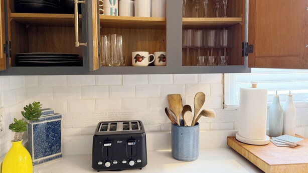 Eine Küche mit einem Toaster, Holzkochlöffeln, einer Vase und einem Schrank mit Geschirr und Gläsern.
