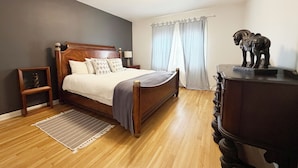 Ein Schlafzimmer mit einem hölzernen Bett, einem Nachttisch, einer Kommode, einem Teppich und einer Wandleuchte.