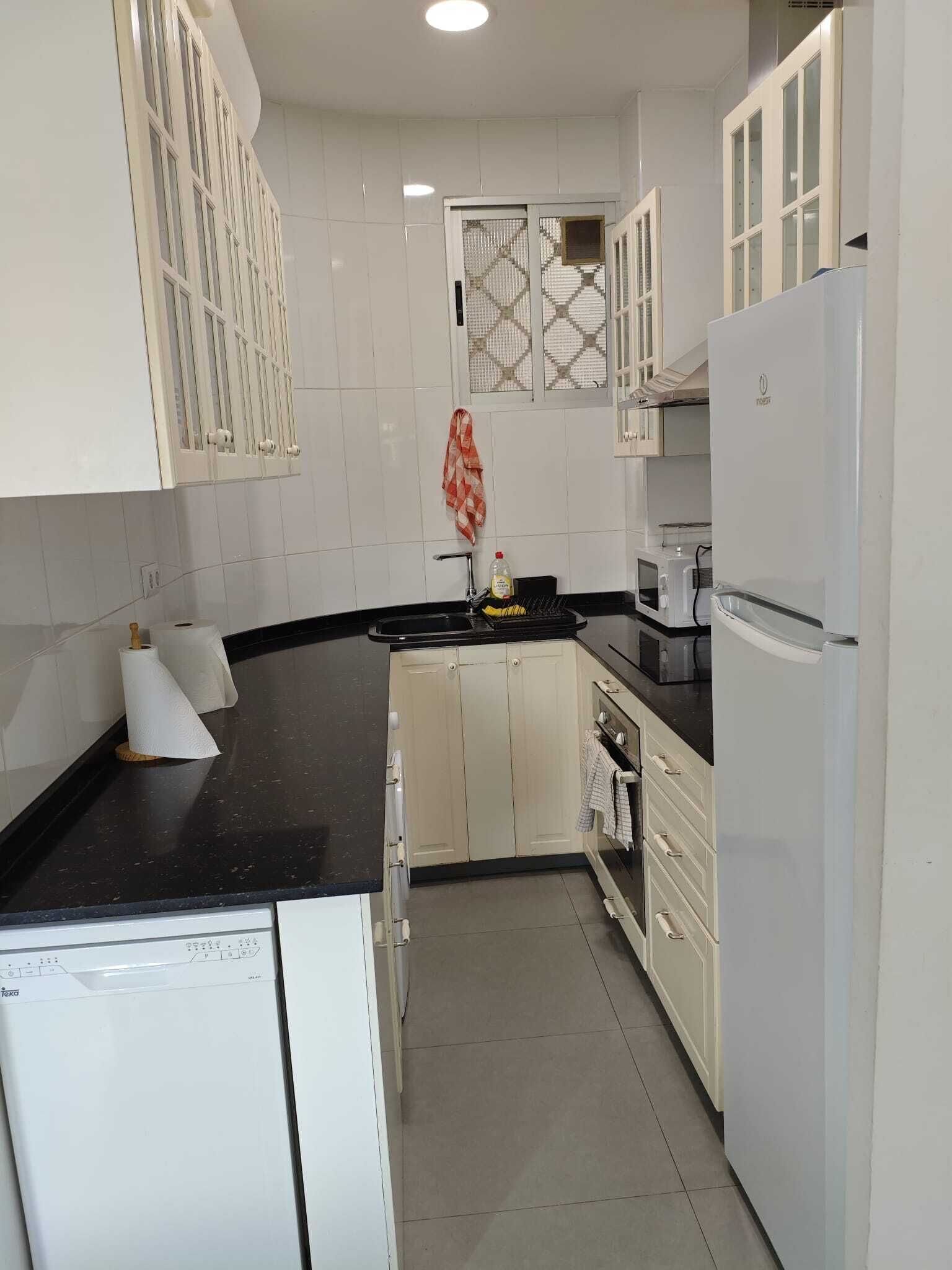A kitchen with white cabinets, a black countertop, a built-in oven, and a refrigerator.
