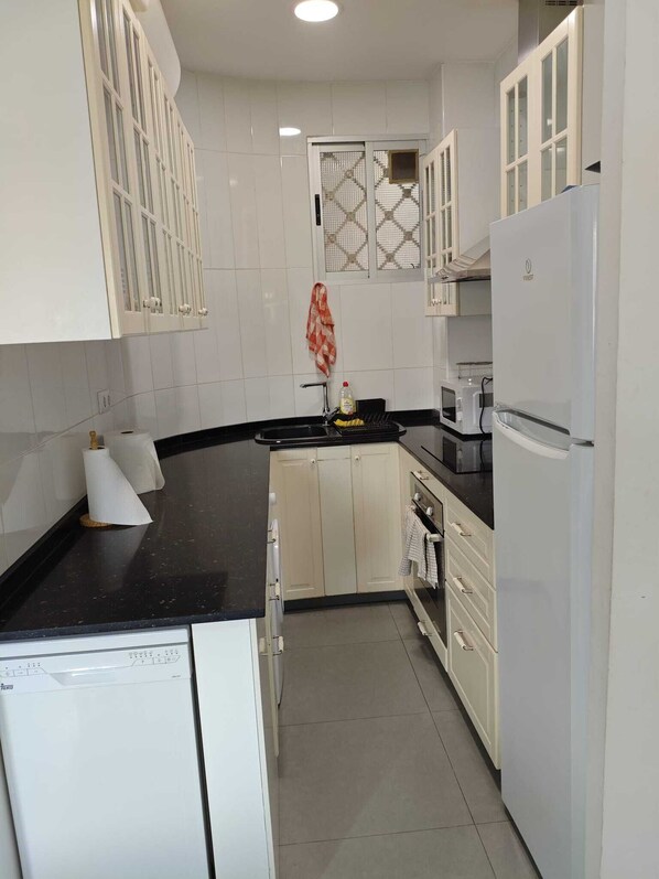 A kitchen with white cabinets, a black countertop, a built-in oven, and a refrigerator.