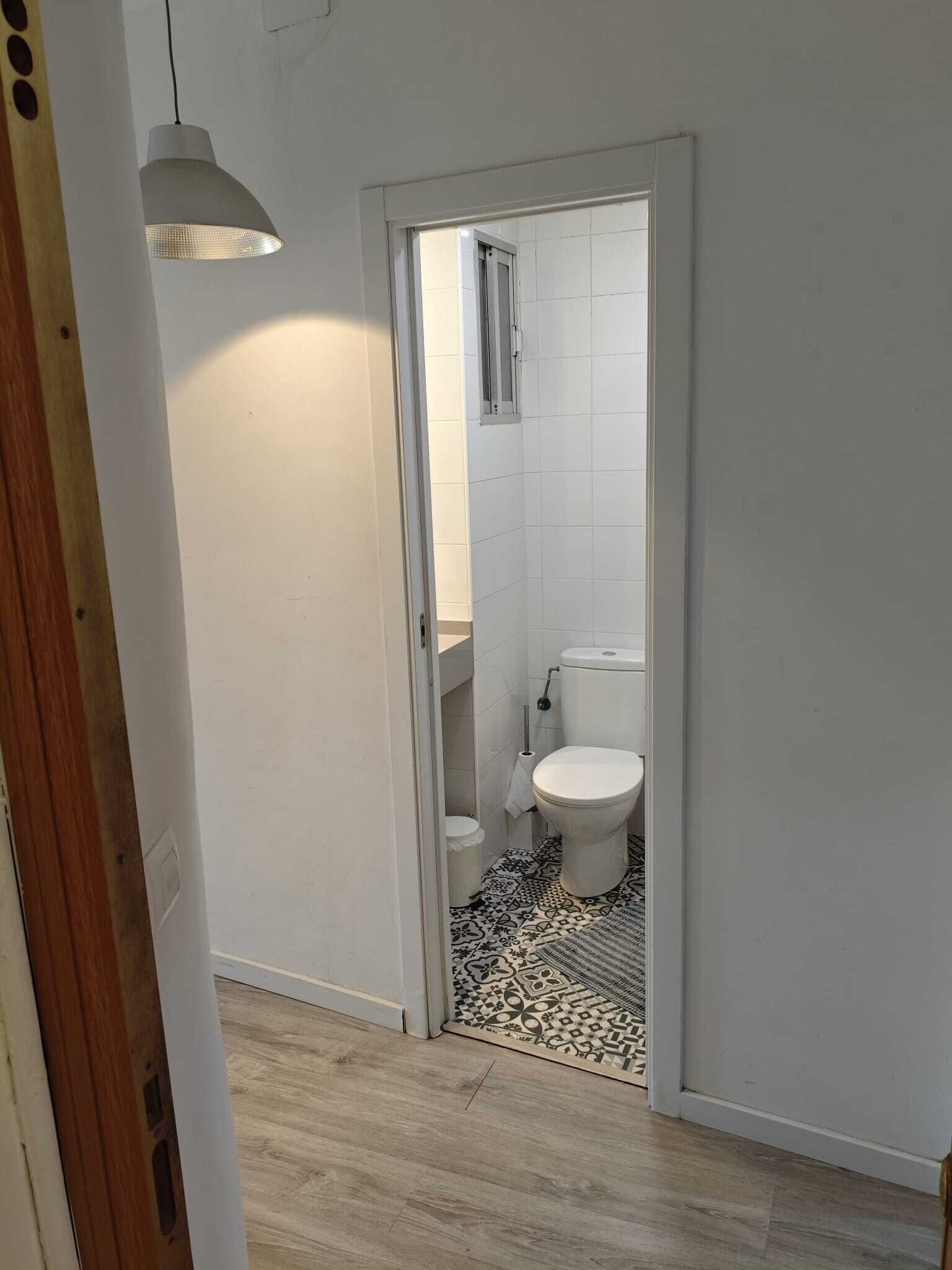 Un pasillo estrecho que conduce a un baño con inodoro, una ventana pequeña y un suelo estampado.