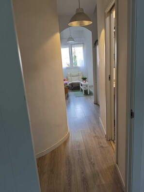 A hallway with wooden flooring, a white sofa, a small table with a plant, and a hanging light fixture.
