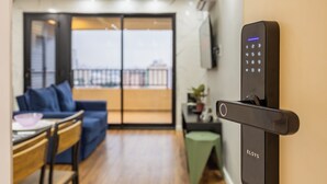 Ein modernes Wohnzimmer mit einer Schiebetür zum Balkon, einem Essbereich und einem schwarzen elektronischen Gerät an der Wand.