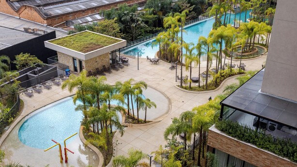 Ein Poolbereich auf dem Dach mit mehreren Pools, umgeben von Palmen und Grünpflanzen, und ein Gebäude mit einer begrünten Dachfläche.