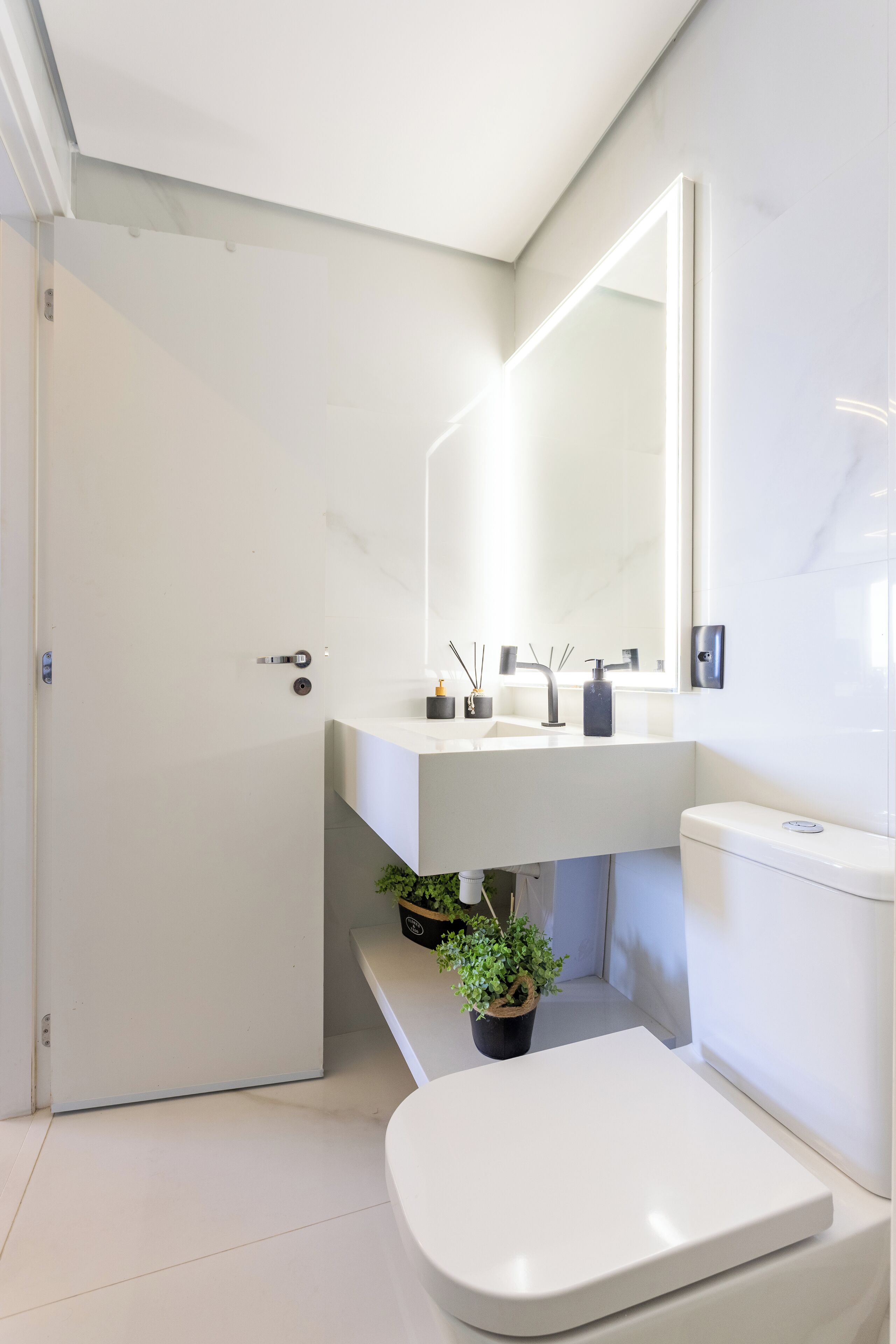 Ein modernes Badezimmer mit einem weißen Waschbecken, Spiegel und WC. Auf dem Boden steht ein kleiner Blumentopf.