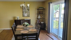 A dining area with a table set for four, surrounded by chairs, a chandelier, and a bookshelf with decorative items.