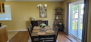 A dining area with a table set for four, surrounded by chairs, a chandelier, and a bookshelf with decorative items. - Entire House by beautiful Georgian Bay (Wiarton)