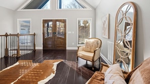 Une pièce spacieuse avec un plafond haut, un grand miroir, une chaise en bois et un tapis en peau de vache.