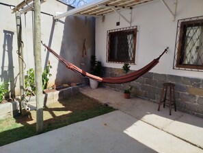 Un hamac dans une cour, avec un mur de pierre, des plantes en pot et un tabouret en bois.