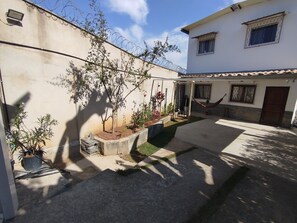 Une cour avec un hamac, des plantes en pot et un petit arbre.