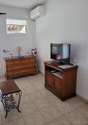 A room with a wooden dresser, a television on a stand, a small table, and a window with blinds. - Quiet studio in Biot (Biot)