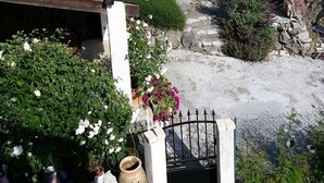 Un sentiero in pietra conduce a un edificio con tetto in tegole, circondato da vegetazione e un muro di pietra.