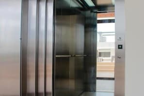 An elevator with a metallic finish and a control panel with a downward arrow. - Gama 09 Apartments - Apartment with balcony (TULUM)