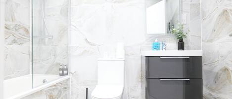 A modern bathroom with a glass shower enclosure, a white toilet, and a grey vanity with a mirror.