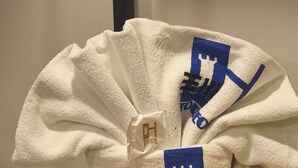 A white bathrobe with a blue logo on a wooden bench. - HOTEL TORREON (Mexico City)
