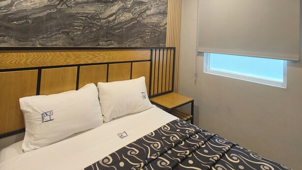A bedroom with a bed, pillows, a headboard, a bedside table, a window with blinds, and a ceiling fan. - HOTEL TORREON (Mexico City)