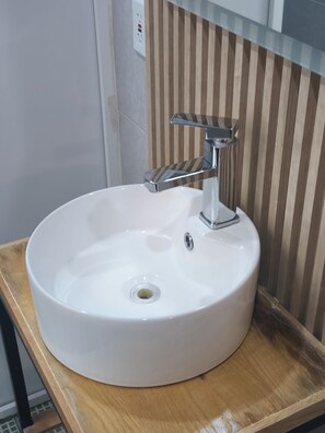 Ein weißes Waschbecken mit modernem Wasserhahn auf einer Holzausziehtheke.