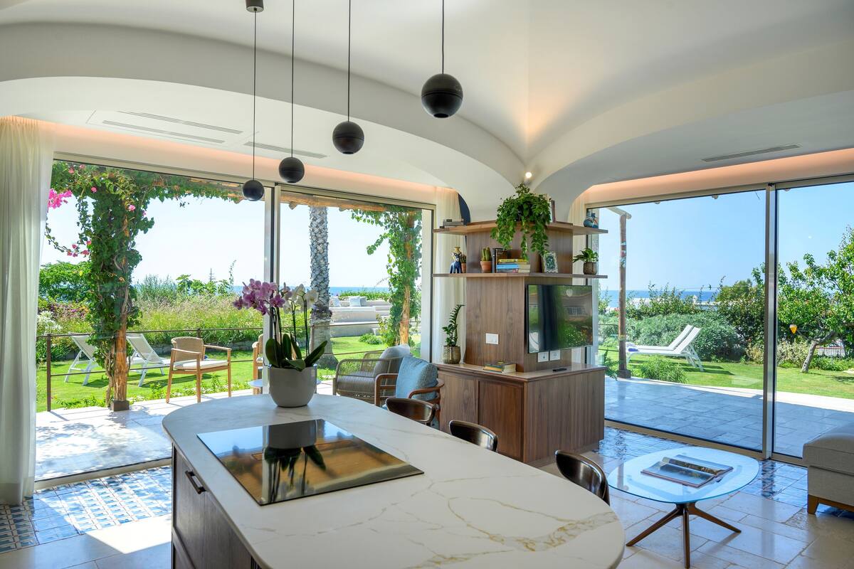 A modern kitchen with a marble countertop, a built-in oven, and a large window overlooking a garden.