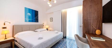 Habitación de hotel con una cama grande, un escritorio, una silla, una lámpara, un cuadro y vistas al exterior.