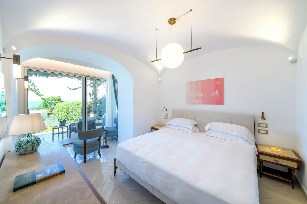 Une chambre moderne avec un grand lit, un bureau, une chaise et une vue sur l’extérieur.