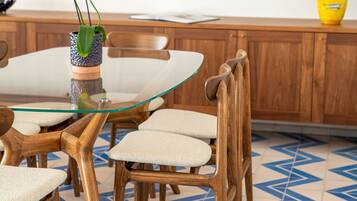 A dining area with a glass table surrounded by wooden chairs, a patterned floor, and a wooden cabinet in the background.