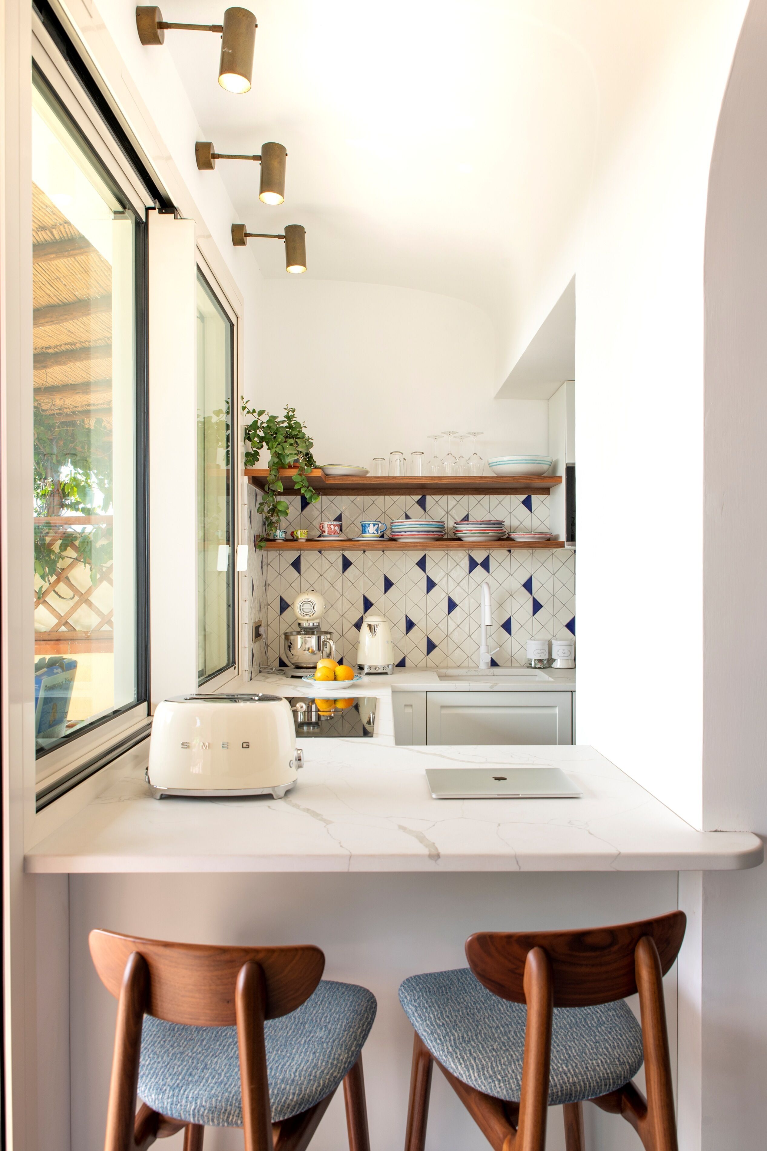 Una cocina moderna con encimera blanca, dos sillas de madera, un tostador, una tetera y un ordenador portátil.