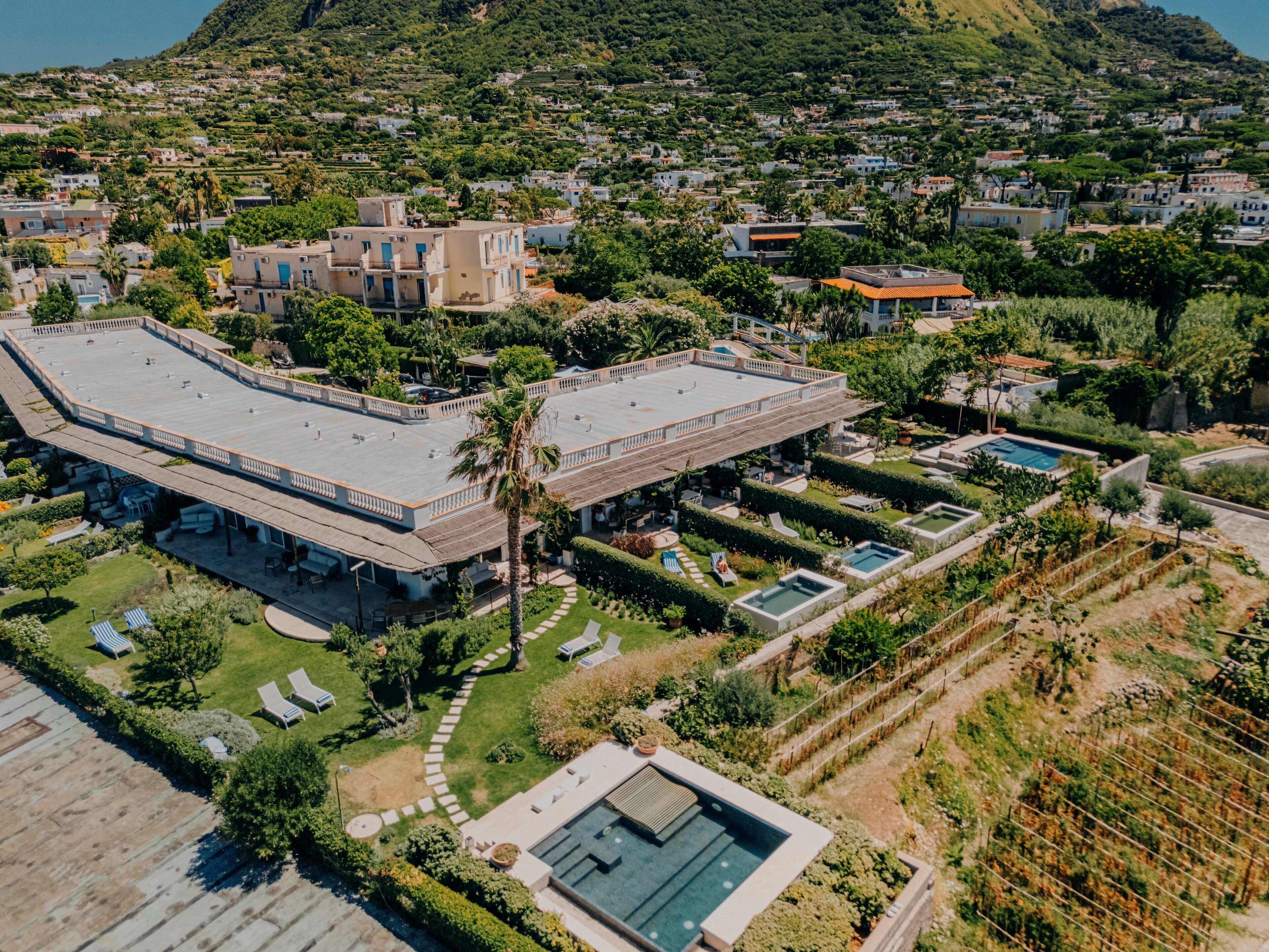 Vista aérea de un resort con varias construcciones, una gran piscina y exuberante jardinería.