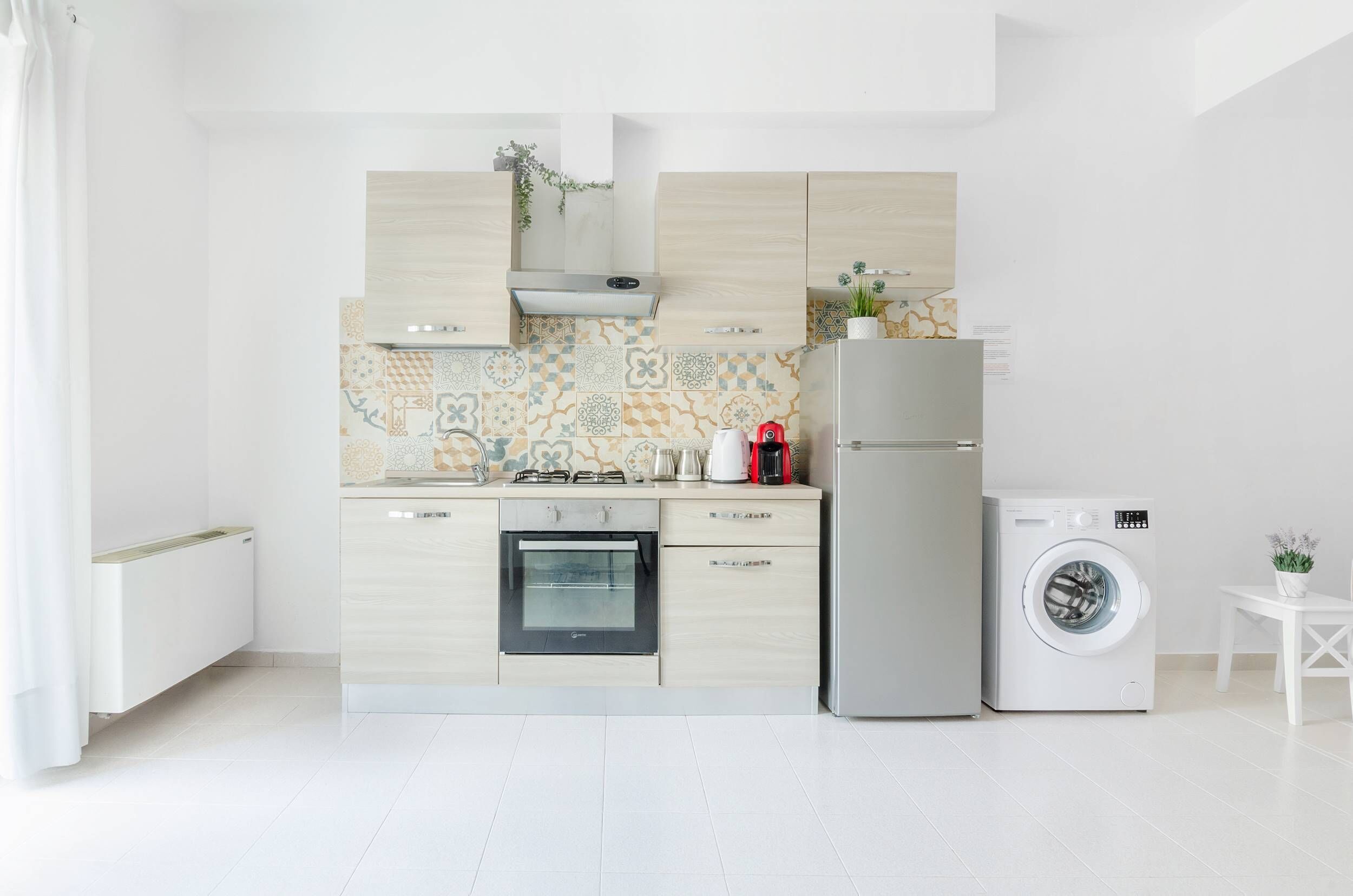 Una cocina moderna con horno empotrado, lavadora y una pequeña mesa con una planta.