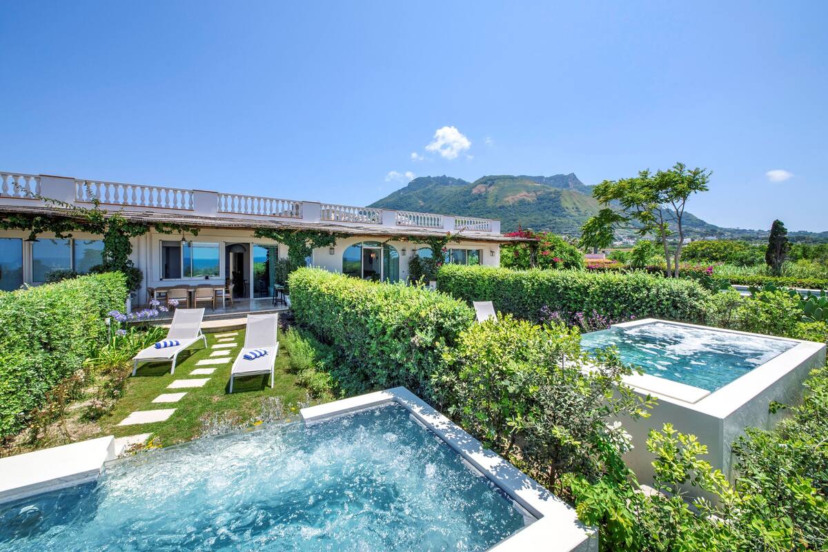 A luxurious outdoor pool area with two separate pools, lounge chairs, and a well-maintained garden.