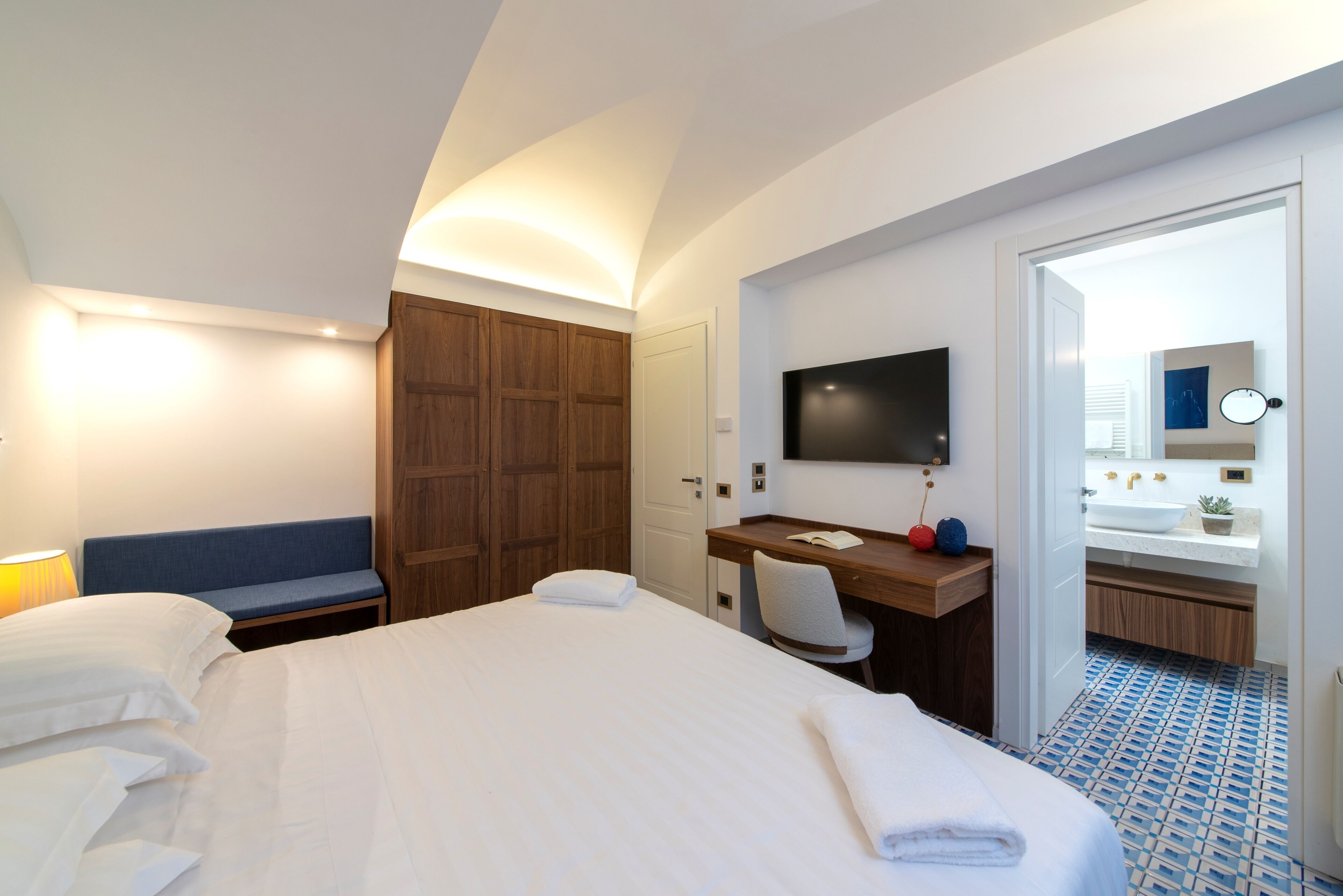 A hotel room with a large bed, a desk with a chair, a television, and a bathroom visible through an open door.