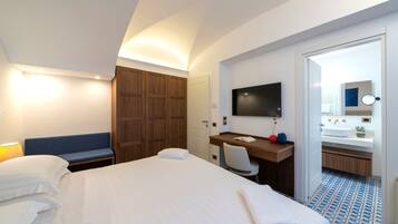 A hotel room with a large bed, a desk with a chair, a television, and a bathroom visible through an open door.