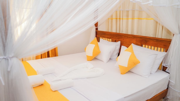 A neatly made bed with white and yellow bedding, a wooden headboard, and a canopy. - Zeylon Villa Talalla (Talalla)