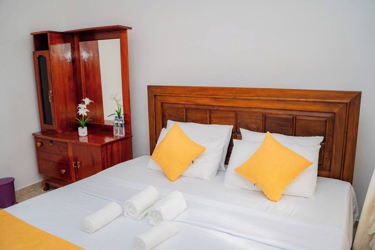 A hotel room with a wooden headboard, white bedding, and two yellow pillows.