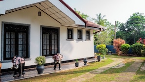 A white building with a red roof and black-framed windows. There are potted plants and a stone pathway in the front yard. - Zeylon Villa Talalla (Talalla)
