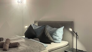 Un dormitorio moderno con cama, almohadas, lámpara de noche y una lámpara colgante.