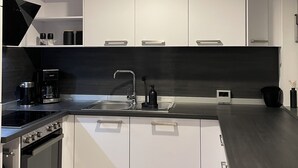 Una cocina moderna con armarios blancos, encimera negra, horno empotrado y cafetera.