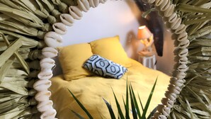 A mirror with a decorative frame, reflecting a bed with yellow bedding and a patterned pillow. - Gîte Bonaty – Comfortable, Quiet, Cozy Furnished Home for 2 to 9 Guests (Soulgé-sur-Ouette)